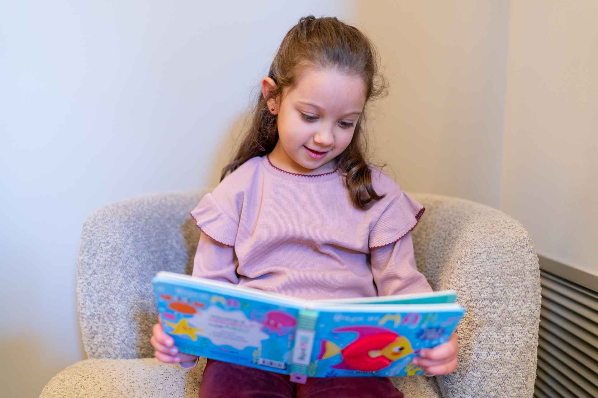 nina pequena sentada leyendo un libro infantil